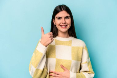 Mavi arka planda izole edilmiş genç beyaz kadın karnına dokunuyor, nazikçe gülümsüyor, yemek yiyor ve tatmin oluyor..