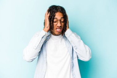 Genç Afrikalı Amerikalı adam mavi arka planda izole edilmiş kulakları elleriyle kapatıyor..