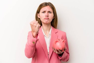 Beyaz arka planda izole edilmiş bir kumbarayı tutan genç İngiliz kadın kameraya yumruk gösteriyor, agresif bir yüz ifadesi..