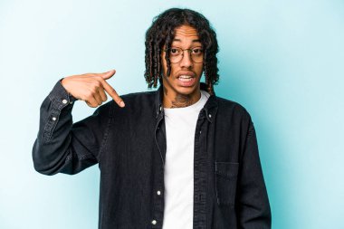 Genç Afrikalı Amerikalı bir adam mavi arka planda izole edilmiş. Elle bir gömlek fotokopi alanını gösteriyor. Gururlu ve kendinden emin.