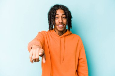 Genç Afro-Amerikalı adam mavi arka planda izole edildi. Neşeli gülümsemeler ön tarafı işaret ediyor..