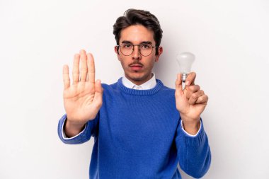 Beyaz arka planda izole edilmiş bir ampul tutan genç beyaz bir adam elini uzatmış, dur işareti göstererek seni engelliyor..