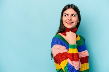 Kafkasyalı genç bir kadın mavi arka planda izole edilmiş başparmak uzakta, gülüyor ve kaygısız.