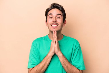 Beyaz tenli genç, bej arka planda izole edilmiş, el ele tutuşmuş, ağzı yakınında dua eden, kendinden emin..