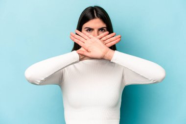 Mavi arka planda izole edilmiş genç beyaz bir kadın inkar jesti yapıyor.