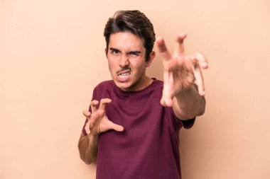 Beyazlı genç bir adam bej arka planda izole edilmiş pençelerini kedi taklidi yaparken gösteriyor, agresif bir hareket..