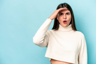 Kafkasyalı genç bir kadın mavi arka planda izole edilmiş, uzaklara bakıyor ve elini alnına koyuyor..