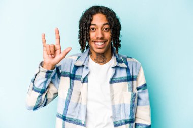 Genç Afrikalı Amerikalı bir adam mavi arka planda izole edilmiş bir şekilde boynuz hareketi bir devrim konsepti olarak gösteriyor..