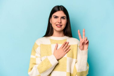 Beyaz bir kadın mavi arka planda izole edilmiş yemin ediyor, elini göğsüne koyuyor..