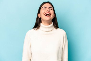 Genç beyaz kadın mavi arka planda izole edilmiş rahat ve mutlu bir şekilde gülüyor, boynunda dişlerini gösteriyor..