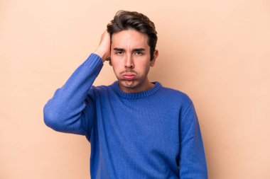 Beyazlı genç bir adam bej arka planda izole edilmiş. Yorgun ve uykulu. Elini başının üstünde tutuyor..