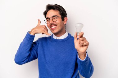 Beyaz arka planda izole edilmiş bir ampul tutan genç beyaz bir adam parmaklarıyla bir cep telefonu hareketi gösteriyor..