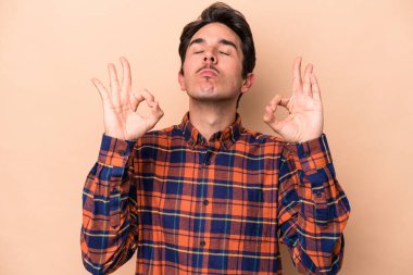 Beyaz tenli genç adam, bej arka planda izole edilmiş yoğun çalışma gününden sonra rahatlıyor, yoga yapıyor..