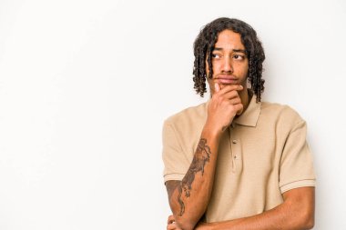 Beyaz arka planda izole edilmiş genç Afrikalı Amerikalı şüpheli ve şüpheci bir ifadeyle yana bakıyor..