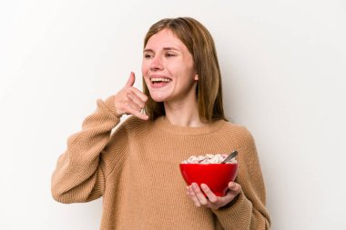 Beyaz arka planda izole edilmiş mısır gevreği yiyen genç bir İngiliz kadın parmaklarıyla bir cep telefonu hareketi gösteriyor..