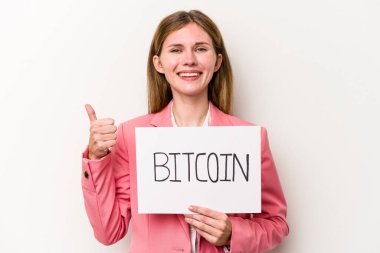 Beyaz arka planda izole edilmiş bitcoin pankartı tutan genç İngiliz iş kadını gülümsüyor ve başparmağını kaldırıyor.