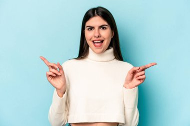 Mavi arka planda izole edilmiş genç beyaz kadın farklı kopya alanlarını gösteriyor, birini seçiyor, parmaklarıyla gösteriyor..