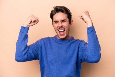 Beyaz tenli genç adam bej arka planda izole edilmiş. Güçlü bir hareket sergiliyor. Kadın gücünün sembolü.