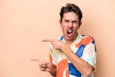 Beyaz tenli genç adam bej arka planda izole edilmiş ve işaret parmağıyla fotokopi alanını işaret ederek heyecan ve arzusunu ifade ediyor..