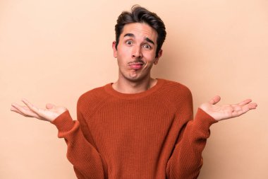 Beyazlı genç bir adam bej arka planda izole edilmiş sorgulama sırasında omuz silkiyor ve şüphe duyuyor..