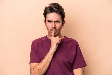 Beyaz tenli genç adam bej arka planda izole edilmiş düşünüyor ve yukarı bakıyor, yansıtıyor, düşünüyor, bir fantezi kuruyor..