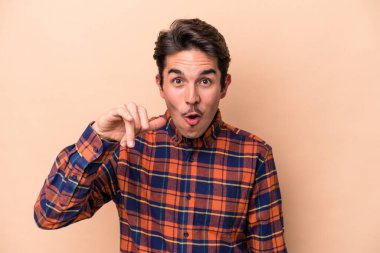 Beyazlı genç bir adam bej arka planda izole edilmiş bir şekilde bir şeye gülüyor, ağzı ellerle örtüyor..