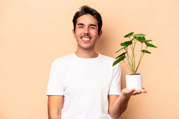 Młody Biały Mężczyzna Gospodarstwa Roślina Odizolowany Beżowy Tło Szczęśliwy Uśmiechnięty — Zdjęcie stockowe