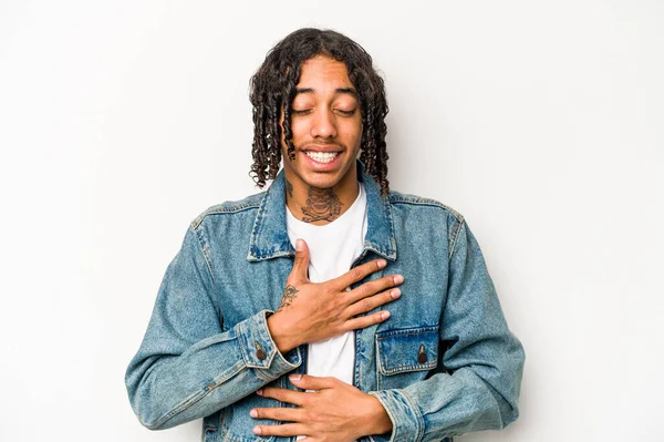 Beyaz arka planda izole edilmiş genç Afrikalı Amerikalı adam mutlu bir şekilde gülüyor ve ellerini karnının üstünde tutarak eğleniyor..