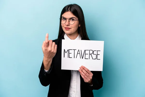 Young caucasian business woman holding a metaverse placard isolated on blue background pointing with finger at you as if inviting come closer.