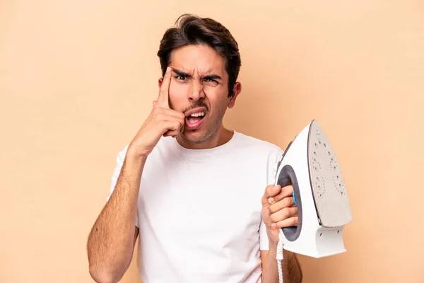 Jonge Blanke Man Met Een Ijzer Geïsoleerd Beige Achtergrond Met — Stockfoto