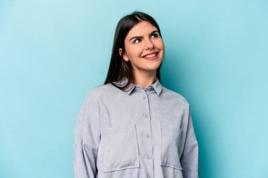 Genç beyaz kadın mavi arka planda izole edilmiş rahat ve mutlu bir şekilde gülüyor, boynunda dişlerini gösteriyor..