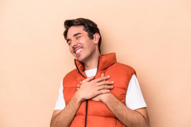Beyazlı genç bir adam bej arka planda izole edilmiş. Gülüyor, elini kalbe koyuyor, mutluluk kavramını koruyor..