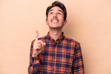 Beyazlı genç bir adam bej arka planda izole edilmiş iki parmağı da boş bir alan gösteriyor..