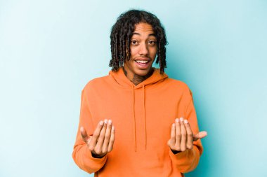 Genç Afro-Amerikalı adam mavi arka planda izole edilmiş, sanki seni davet ediyormuş gibi parmağıyla işaret ediyor..