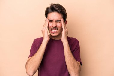 Beyaz tenli genç adam bej arka planda izole edilmiş tapınaklara dokunuyor ve baş ağrısı çekiyor..