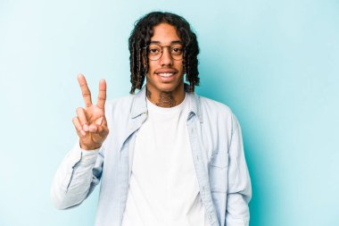 Genç Afrikalı Amerikalı adam mavi arka planda izole edilmiş. İki numarayı parmaklarıyla gösteriyor..