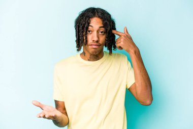 Genç Afrikalı Amerikalı bir adam mavi arka planda izole edilmiş ve elinde bir ürün tutuyor..