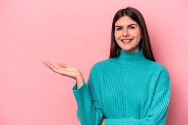 Pembe arka planda izole edilmiş genç beyaz kadın bir avuç içinde fotokopi alanı ve belinde bir el daha gösteriyor..