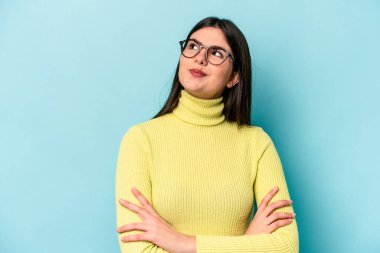 Mavi arka planda izole edilmiş genç beyaz kadın hedeflerine ve amaçlarına ulaşma hayali kuruyor.