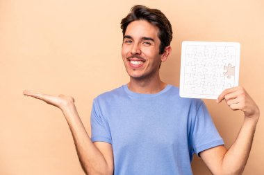 Elinde bej arka planda izole edilmiş bir yapboz tutan genç beyaz bir adam bir avuç içinde fotokopi alanı ve belinde bir el daha olduğunu gösteriyor..