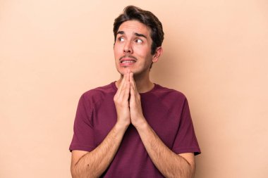 Beyaz tenli genç adam bej arka planda izole edilmiş dua ediyor, bağlılık gösteriyor, dindar biri ilahi ilham arıyor..