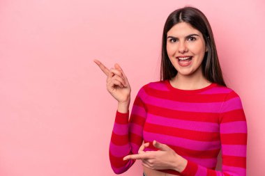 Pembe arka planda izole edilmiş genç beyaz kadın işaret parmaklarıyla işaret ederek heyecanlanıyor..