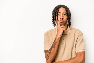 Beyaz arka planda izole edilmiş genç Afrikalı Amerikalı şüpheli ve şüpheci bir ifadeyle yana bakıyor..
