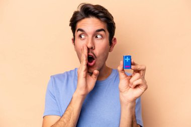 Beyazlı genç bir beyaz adam bej arka planda izole edilmiş bir bateriyi tutuyor ve gizli bir sıcak fren haberini veriyor.