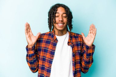 Genç Afrikalı Amerikalı adam mavi arka planda izole edilmiş neşeli bir şekilde gülüyor. Mutluluk kavramı.