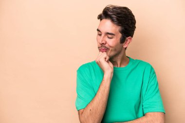 Beyazlı genç adam bej arka planda izole edilmiş şüpheli ve şüpheci bir ifadeyle yana bakıyor..
