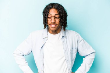 Genç Afro-Amerikalı adam mavi arka planda izole edilmiş. Kendine güvenen, kalçaları tutan..