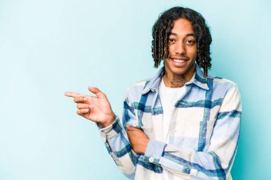 Genç Afrikalı Amerikalı adam mavi arka planda izole edilmiş, mutlu bir şekilde işaret parmağıyla işaret ederek gülümsüyor..