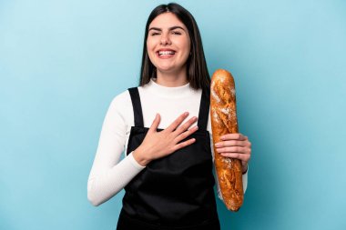 Mavi arka planda bir somun ekmek tutan genç beyaz tenli kahkahalar atıyor..