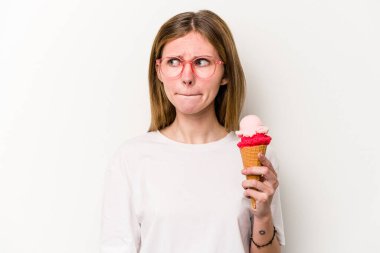 Beyaz arka planda izole edilmiş dondurmayı tutan genç bir İngiliz kadın kafası karışmış, şüpheli ve kendinden emin değil..
